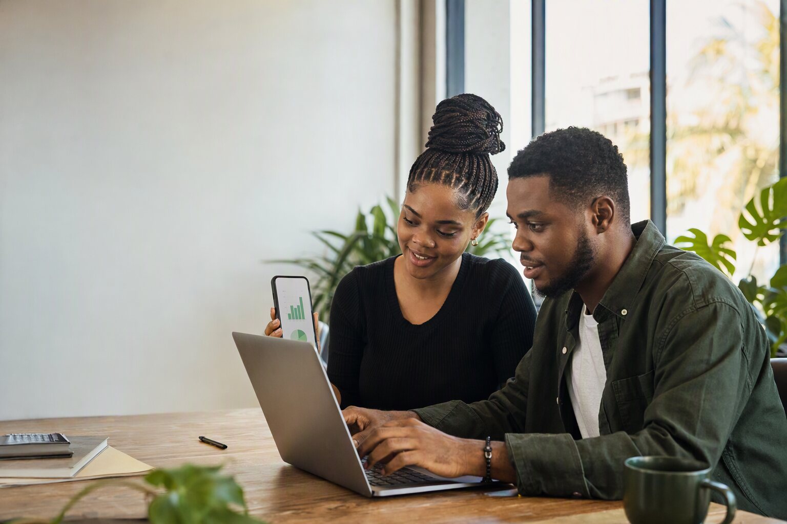 Two young founders testing an AI app on a phone and a laptop in a bright co-working space (generated image)